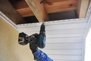 Worker installing roof on the interior side of a house roof using drill machine