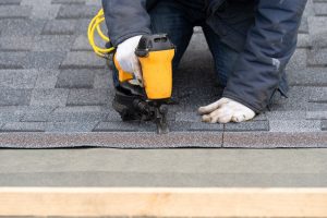 worker nailing asphalt shingles to roof