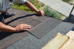 Worker placing asphalt shingles on roof