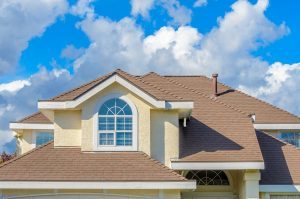 Cloudy sky in the background an a suburban home in the foreground. Home has a brown roofing system.