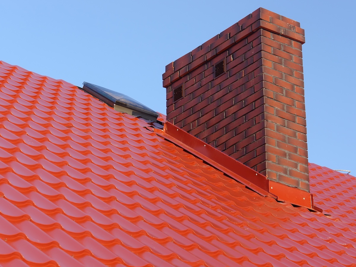 Red metal tile roof with a brick chimney with matching red metal flashing