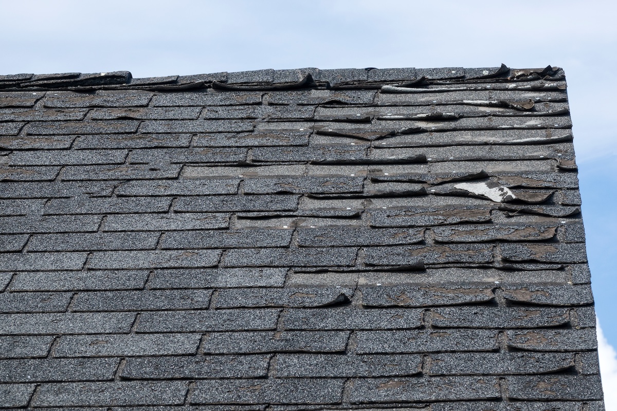 A roof with damaged and warped asphalt shingles