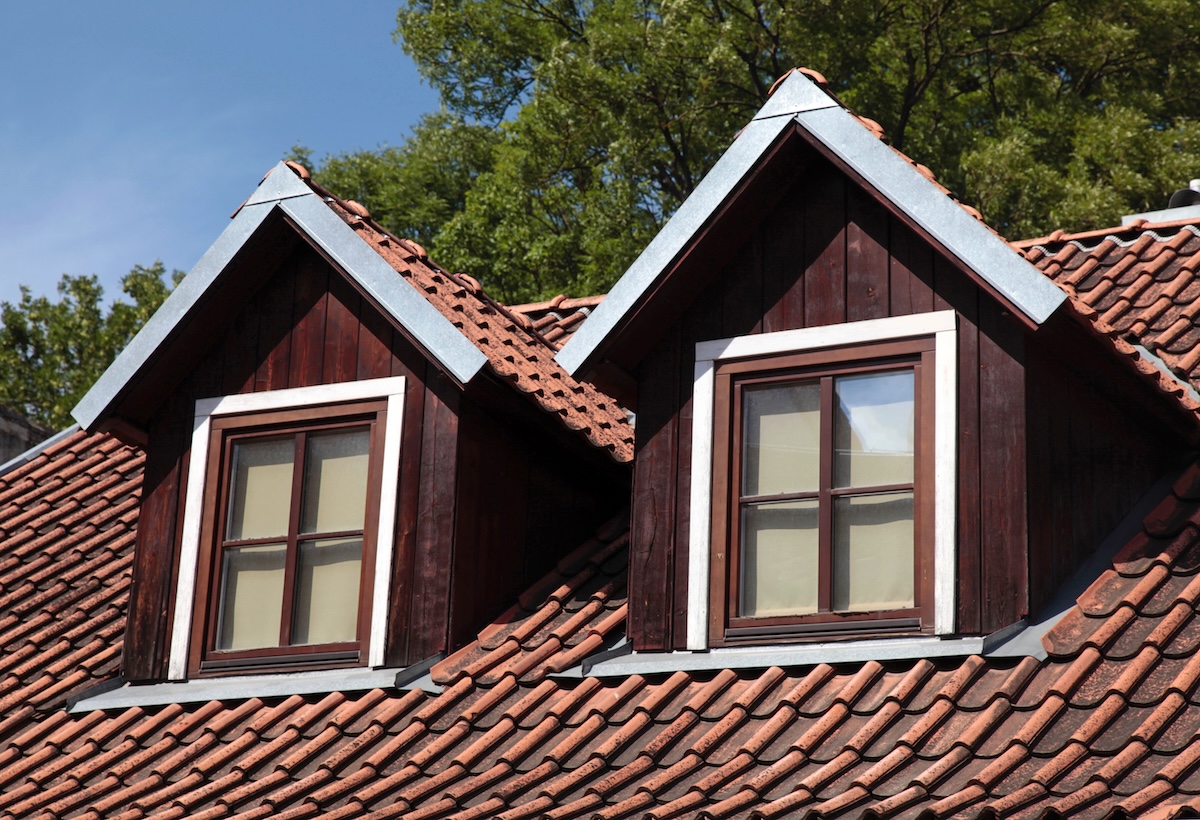 Two wooden dormer windows with white trim protrude from a red tiled roof